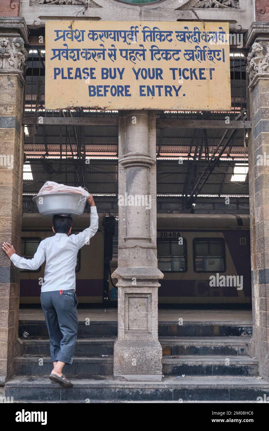 A porter with a basket of fish on his head entering Chhatrapati Shivaji Maharaj Terminus (CMST), in Mumbai, India, to forward the basket by train Stock Photo