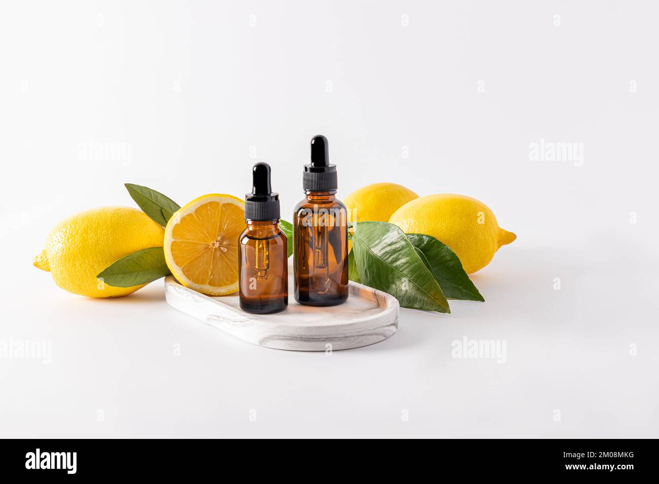 two bottles of dark glass with a dropper with cosmetic bleach stand on a plaster white tray among ripe lemons Stock Photo