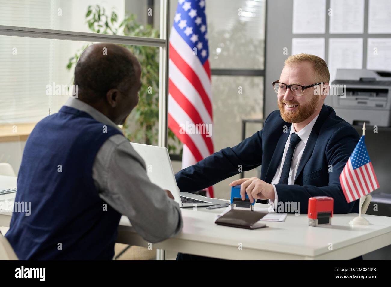 Portrait of friendly smiling worker consulting senior black man in US immigration office Stock Photo
