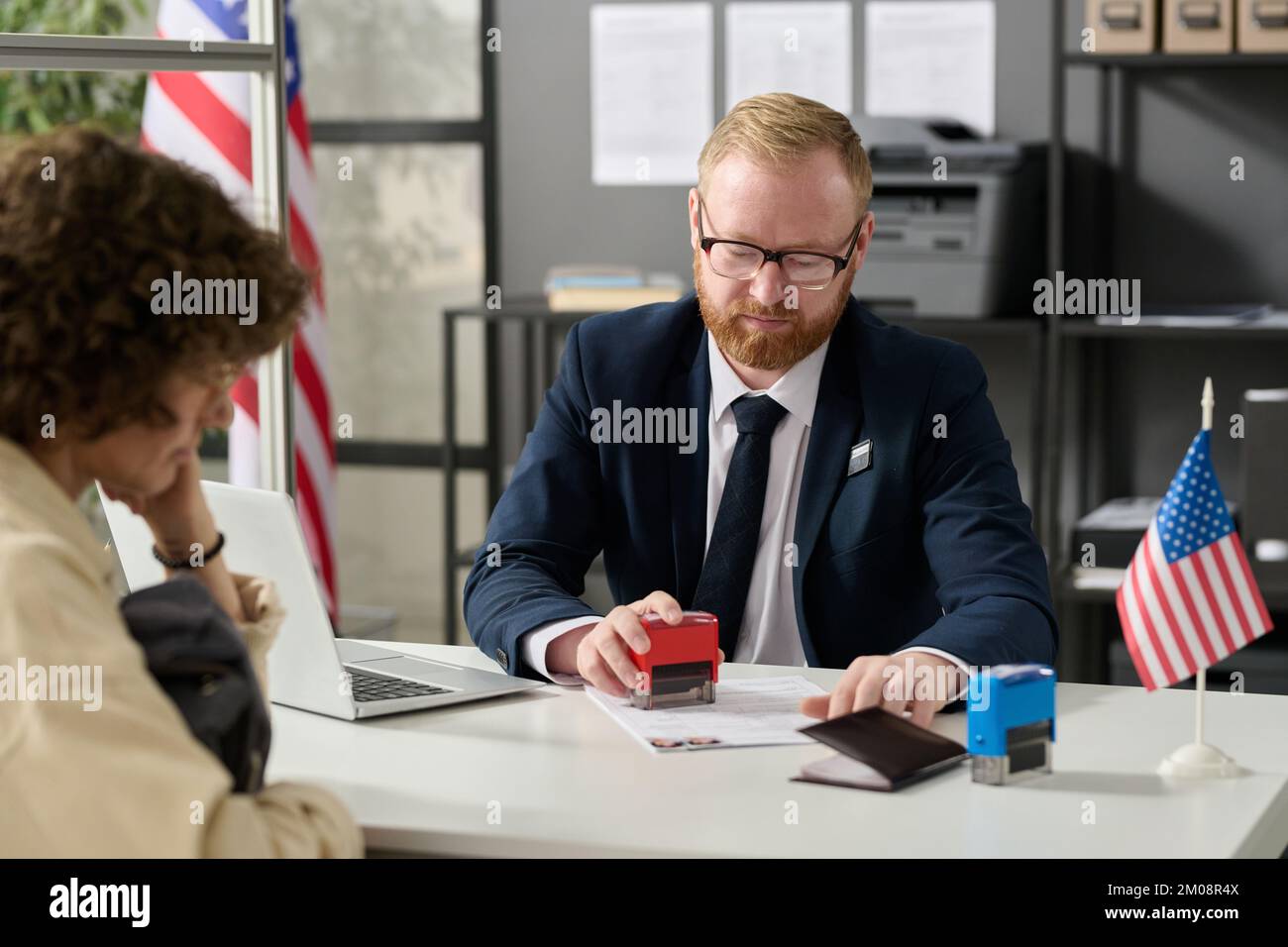 Portrait of immigration office worker stamping application form while working with client in cubicle Stock Photo