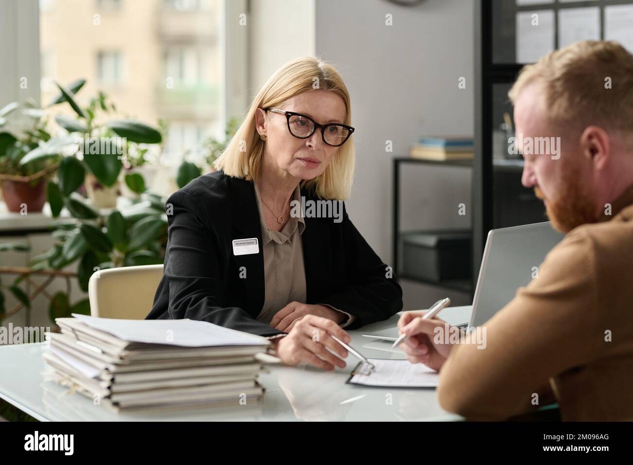 Portrait of mature woman consulting man in insurance agency office and pointing at application forms Stock Photo