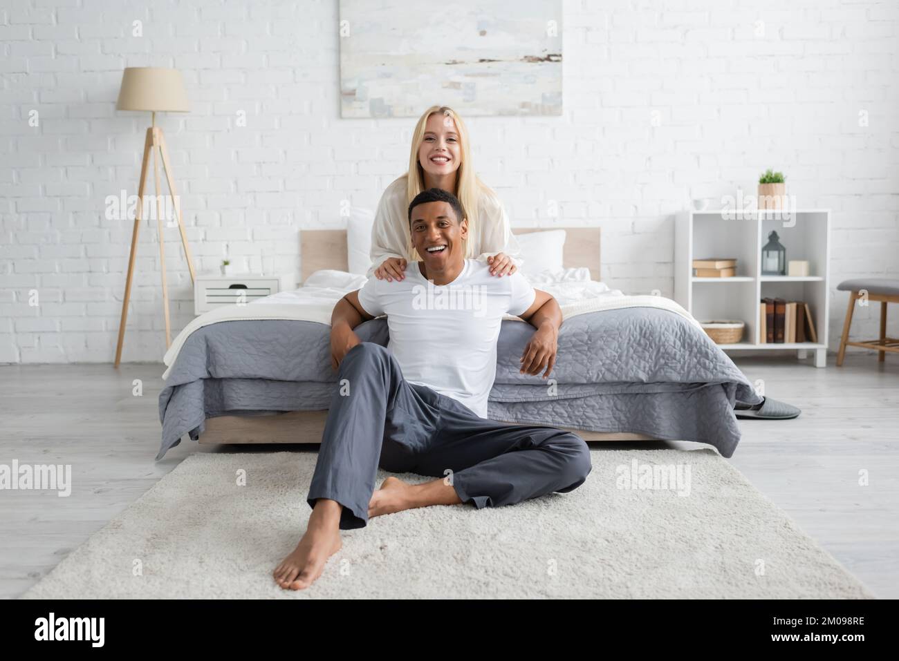cheerful-african-american-man-in-sleepwear-sitting-on-floor-in-bedroom