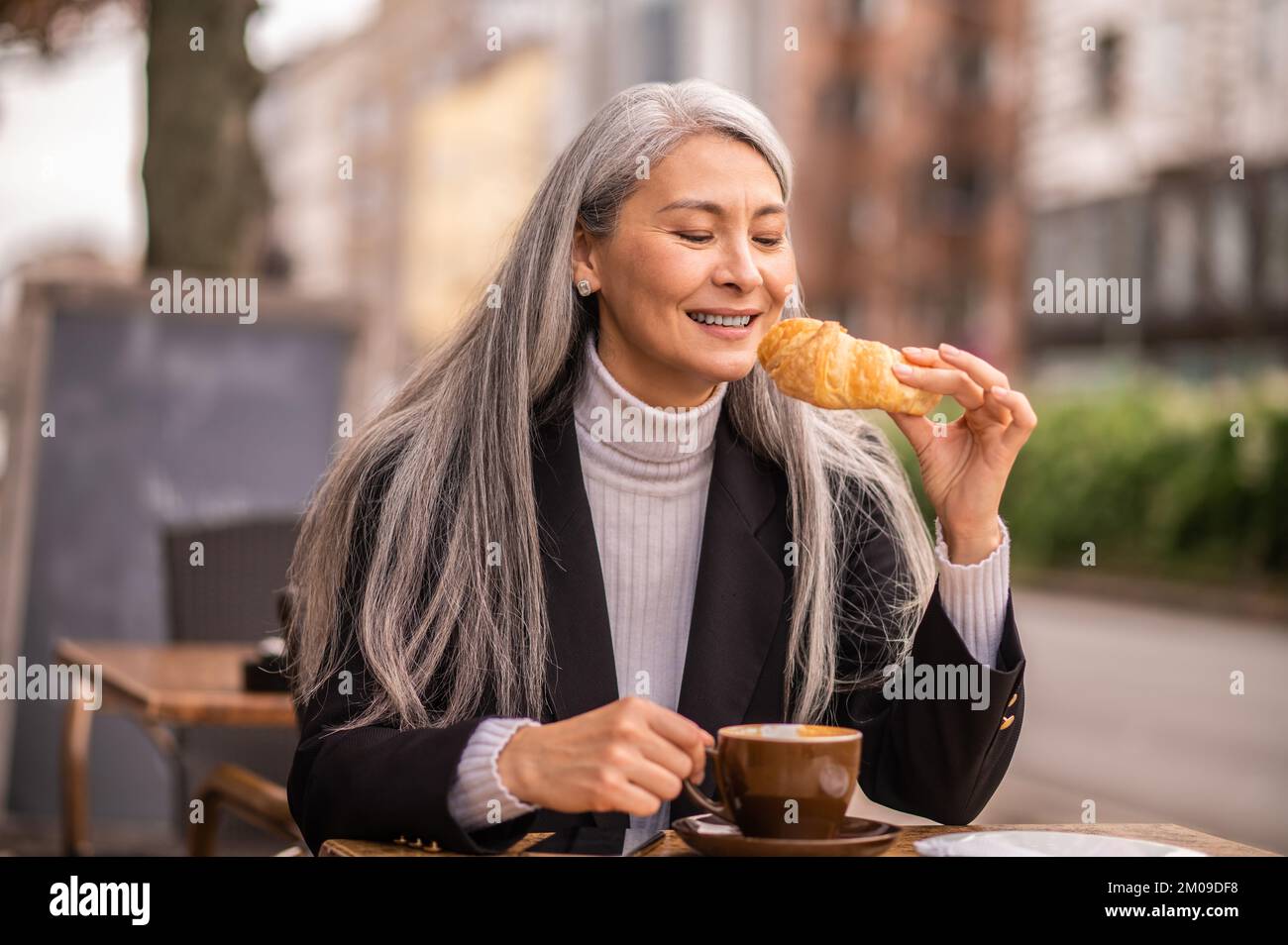 Pretty woman eating croissant and looking contented Stock Photo Alamy