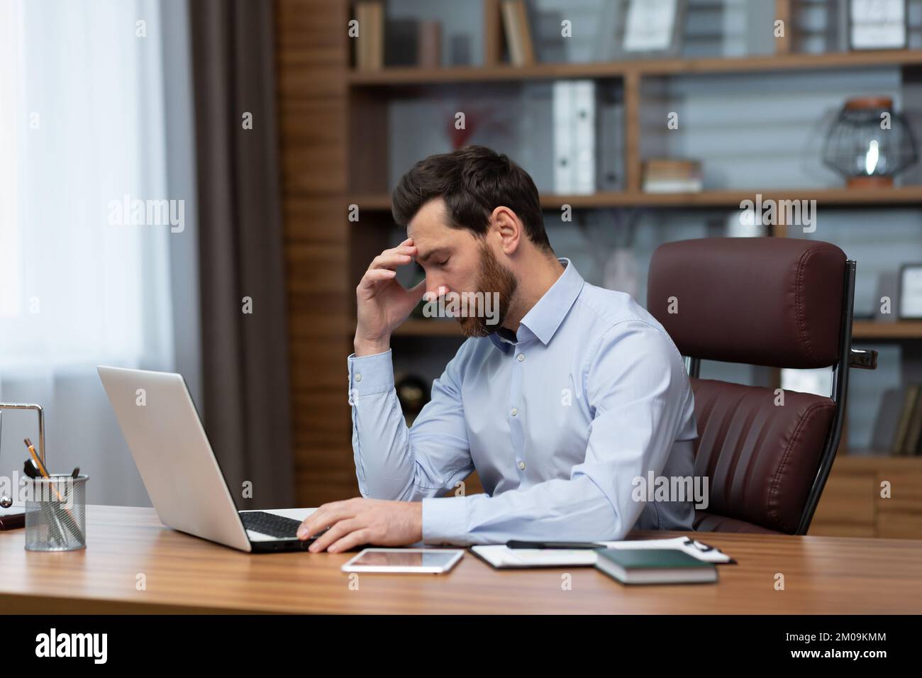 Mature pensive sad businessman working inside office, boss using laptop at work thinking about difficult decision in shirt. Stock Photo