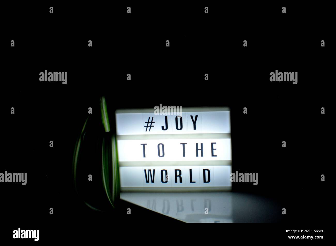 Light box with the phrase, '# Joy to the world' illuminated on it set in shadow and dark background Stock Photo