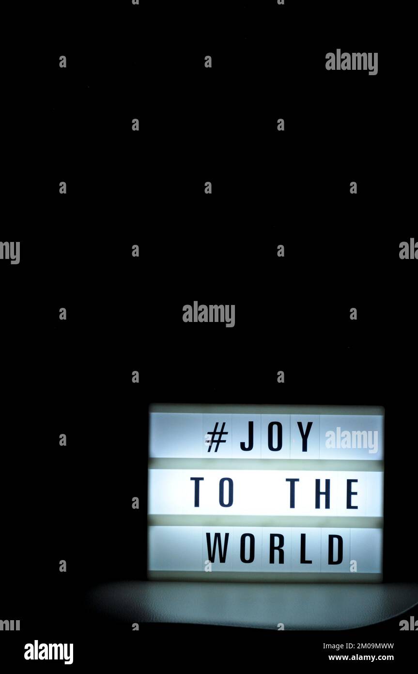 Light box with the phrase, '# Joy to the world' illuminated on it set in shadow and dark background Stock Photo