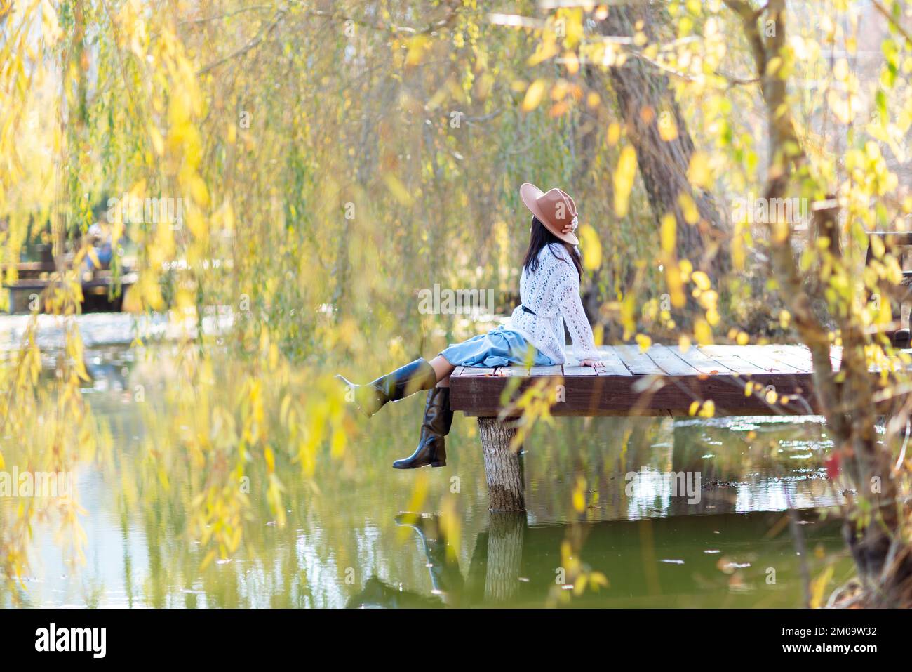 Autumn lake woman. She sits by a pond on a wooden pier in autumn and admires nature. The concept of tourism, weekends outside the city. Stock Photo