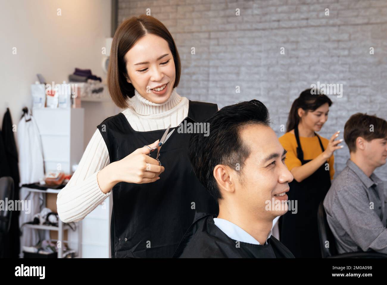 Asian female hairdresser making haircut for two male customer with male