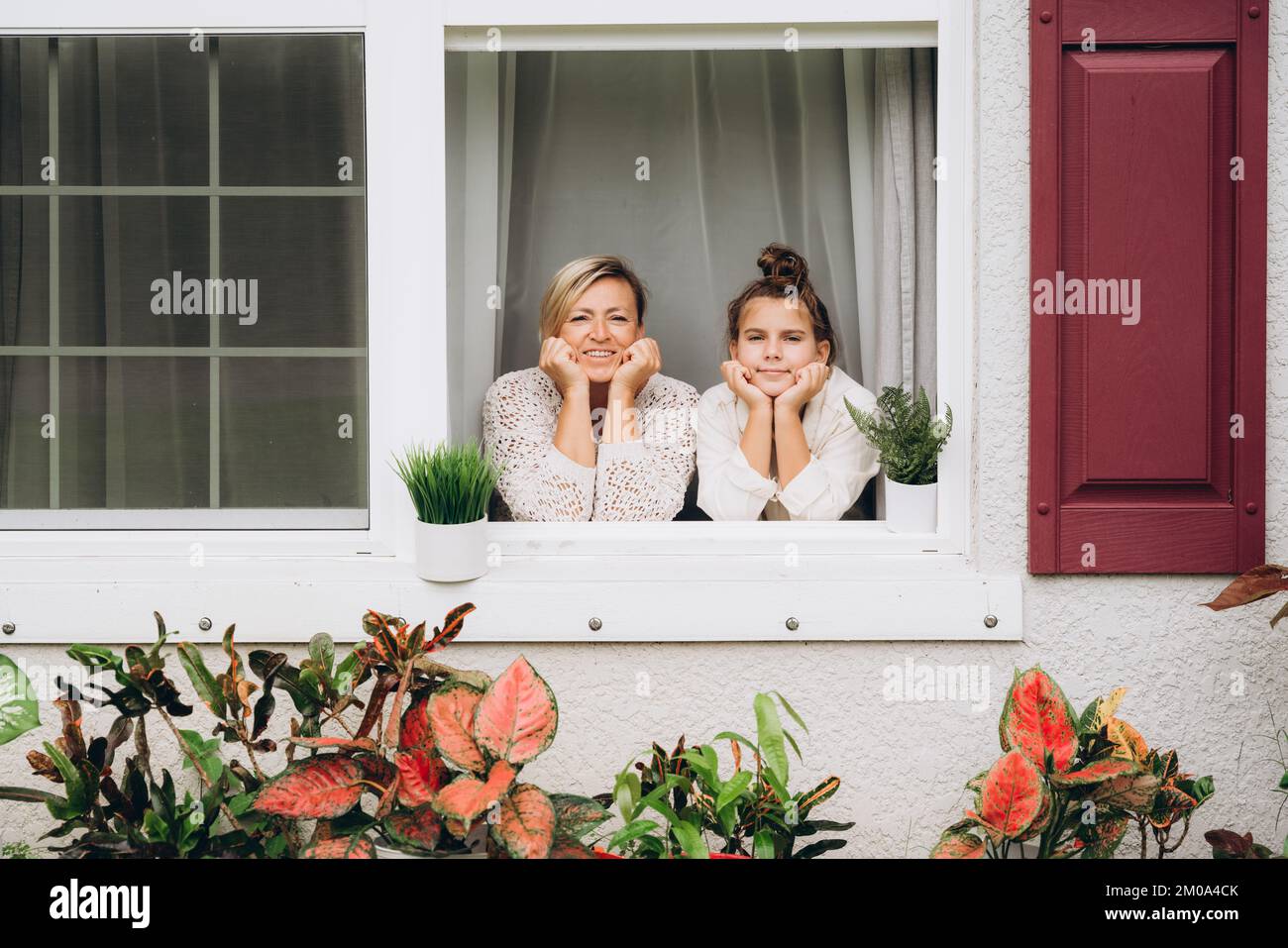 Smiling Mother and daughter in the window looking into the garden Stock Photo