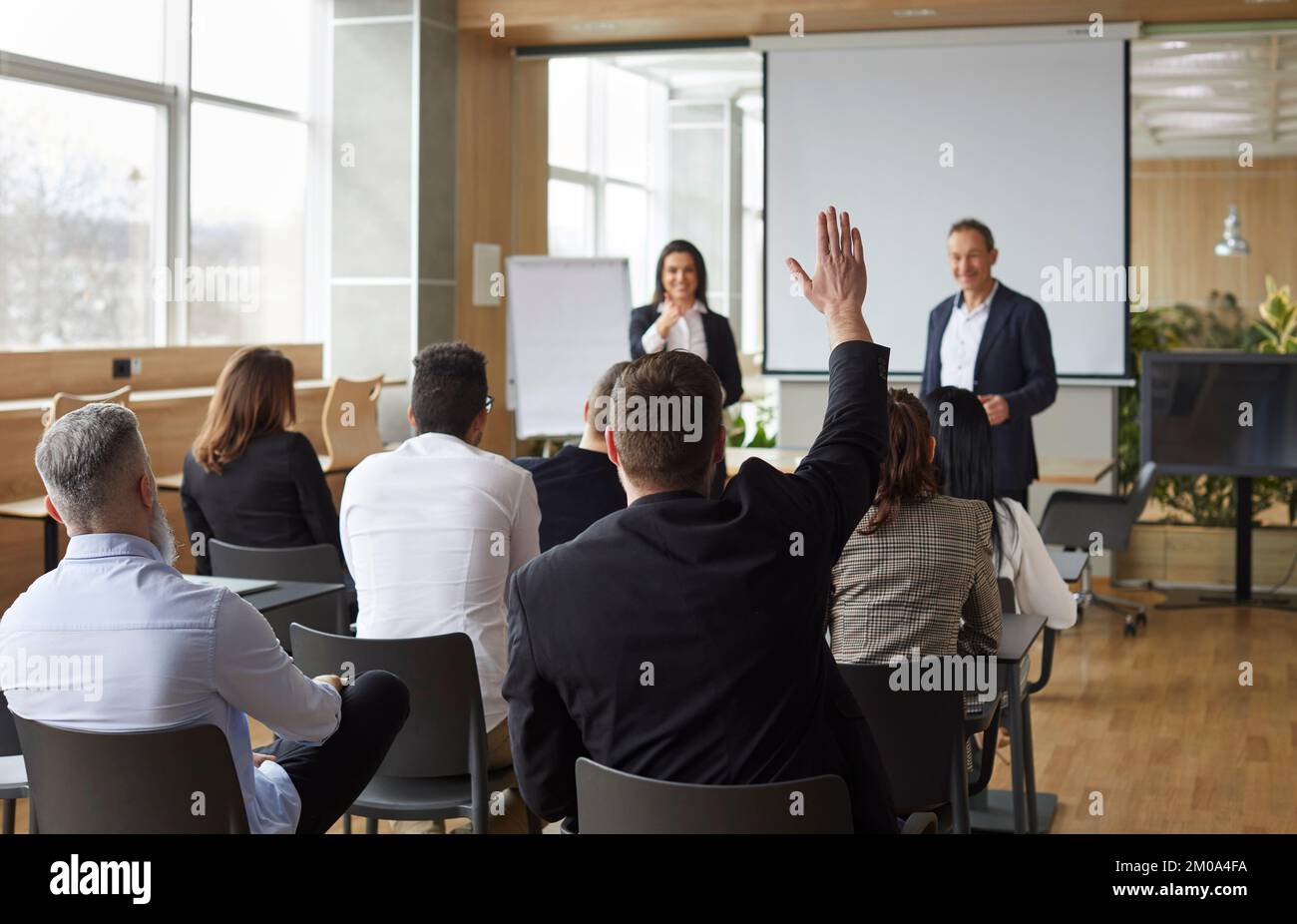 Man with raised hand wants to ask questions or express opinion during business presentation. Stock Photo