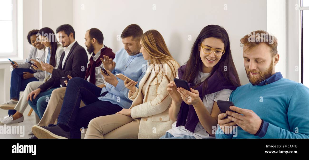 Group of happy young men and women sitting in office and using their smartphones Stock Photo