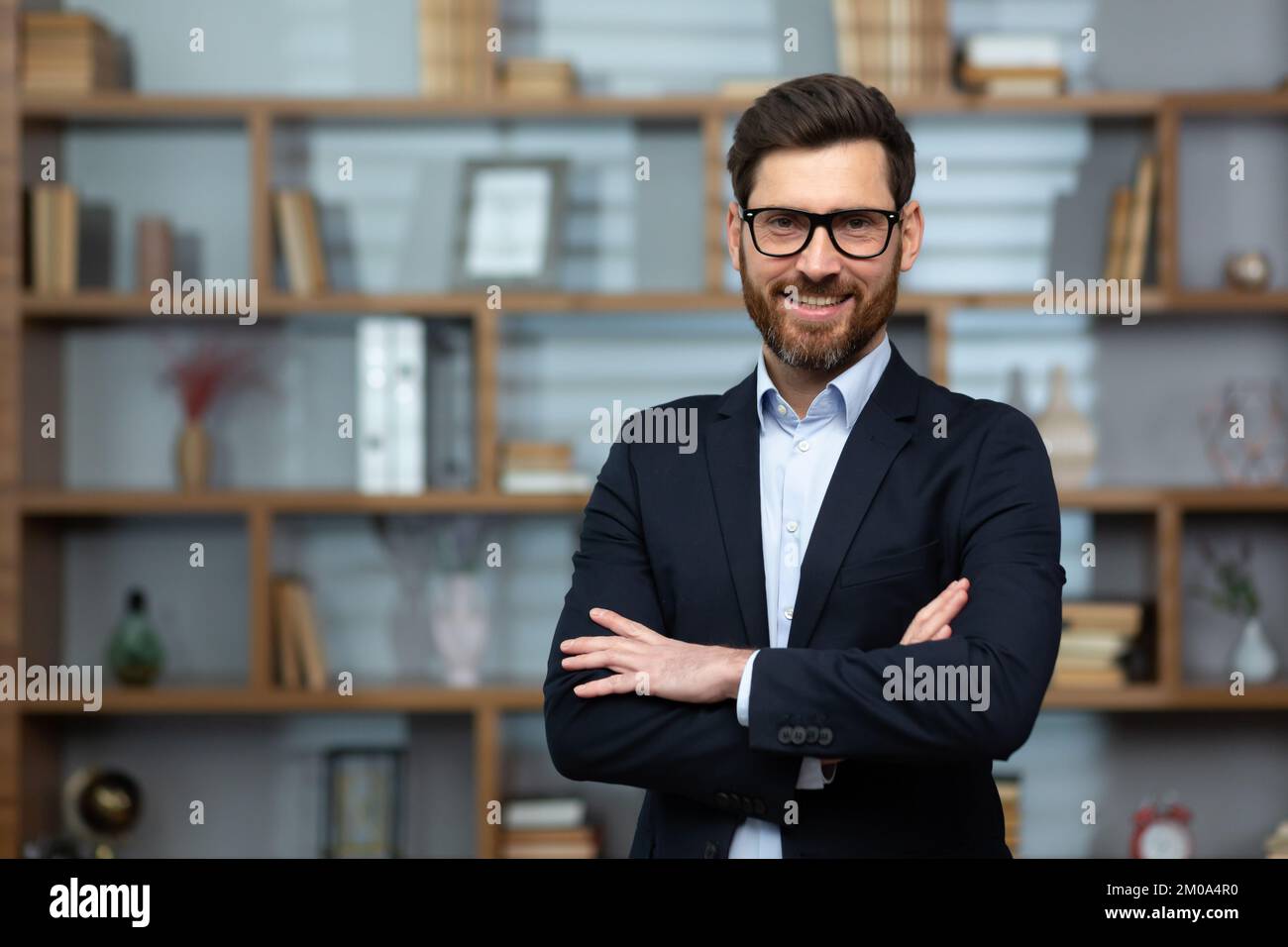 Portrait of successful mature boss, senior businessman in glasses and business suit looking at camera and smiling, man with crossed arms working inside modern office building. Stock Photo