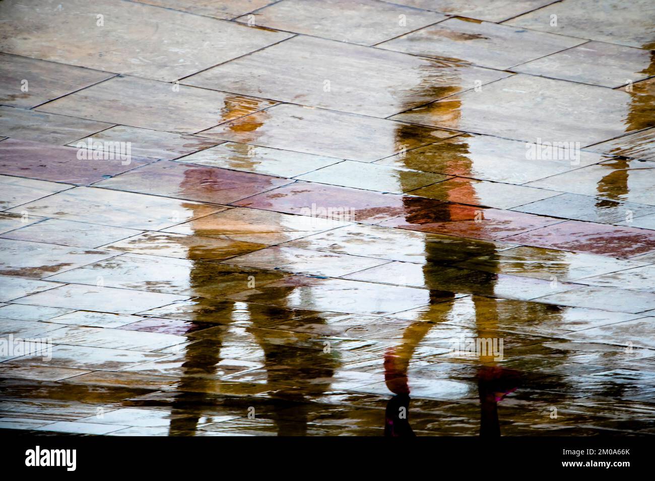 Abstract blurry silhouette shadow reflections of unrecognizable people reflections walking on wet city street pavement on a rainy spring day Stock Photo