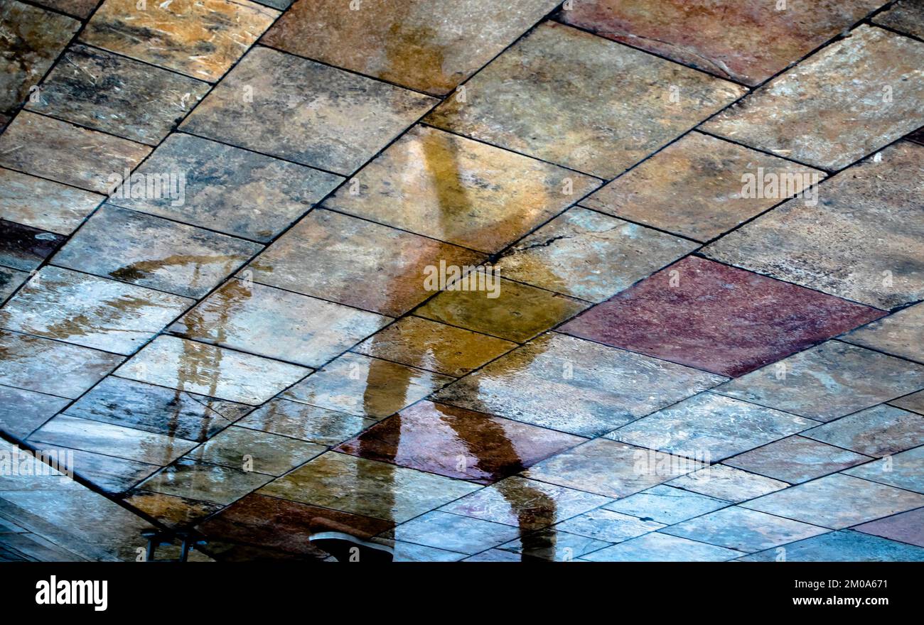 Abstract blurry silhouette shadow reflections of unrecognizable people reflections walking on wet city street pavement on a rainy spring day Stock Photo