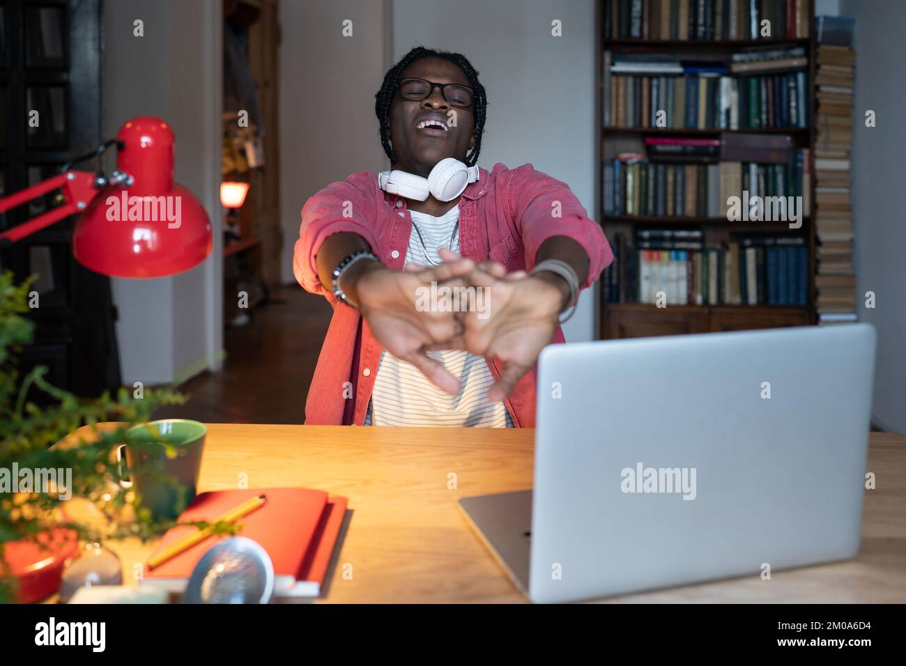 Sleepy African student guy yawning stretching arms while studying on laptop for long hours at home Stock Photo