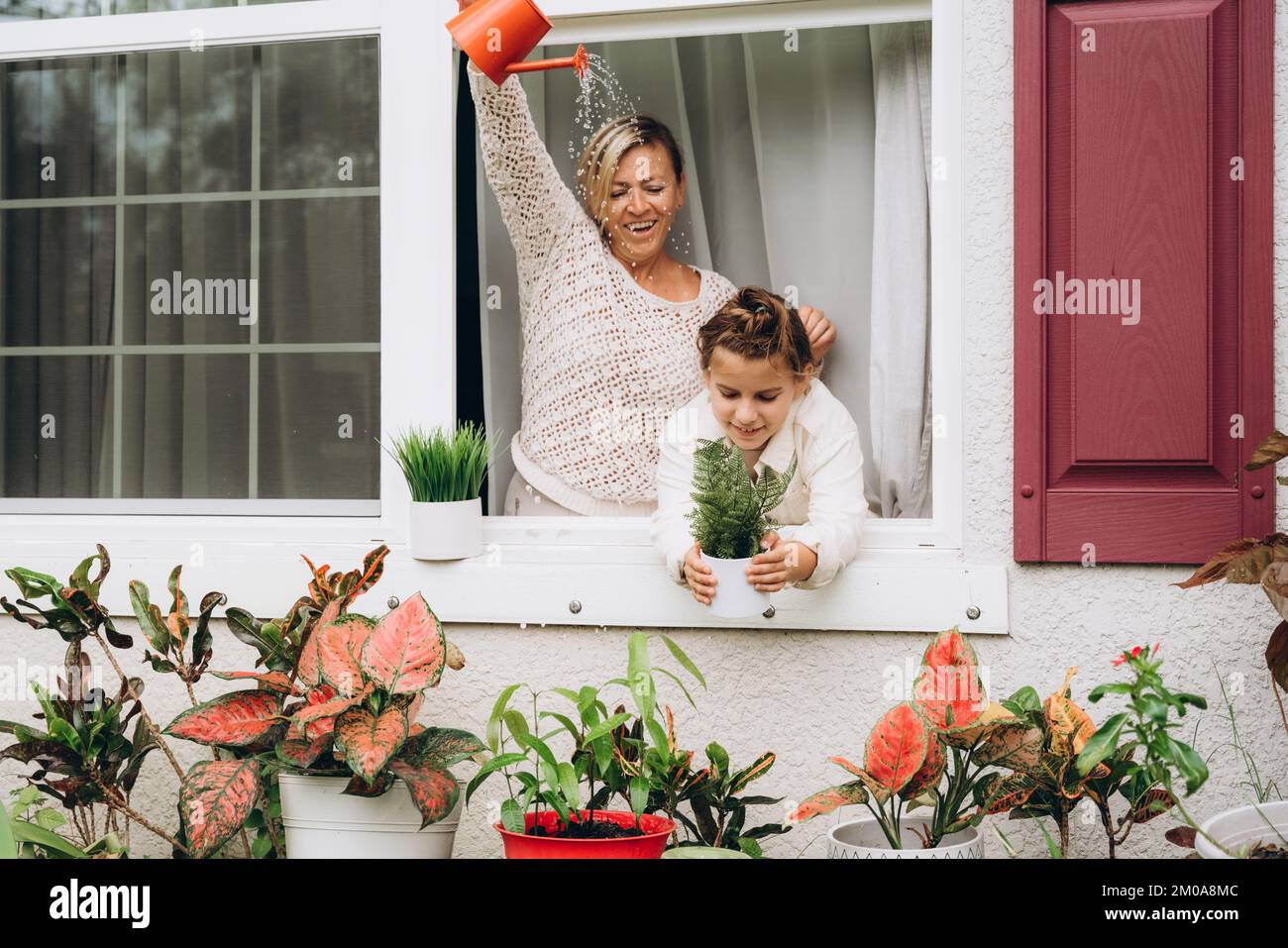 Girl with mom watering plants from a watering can Stock Photo
