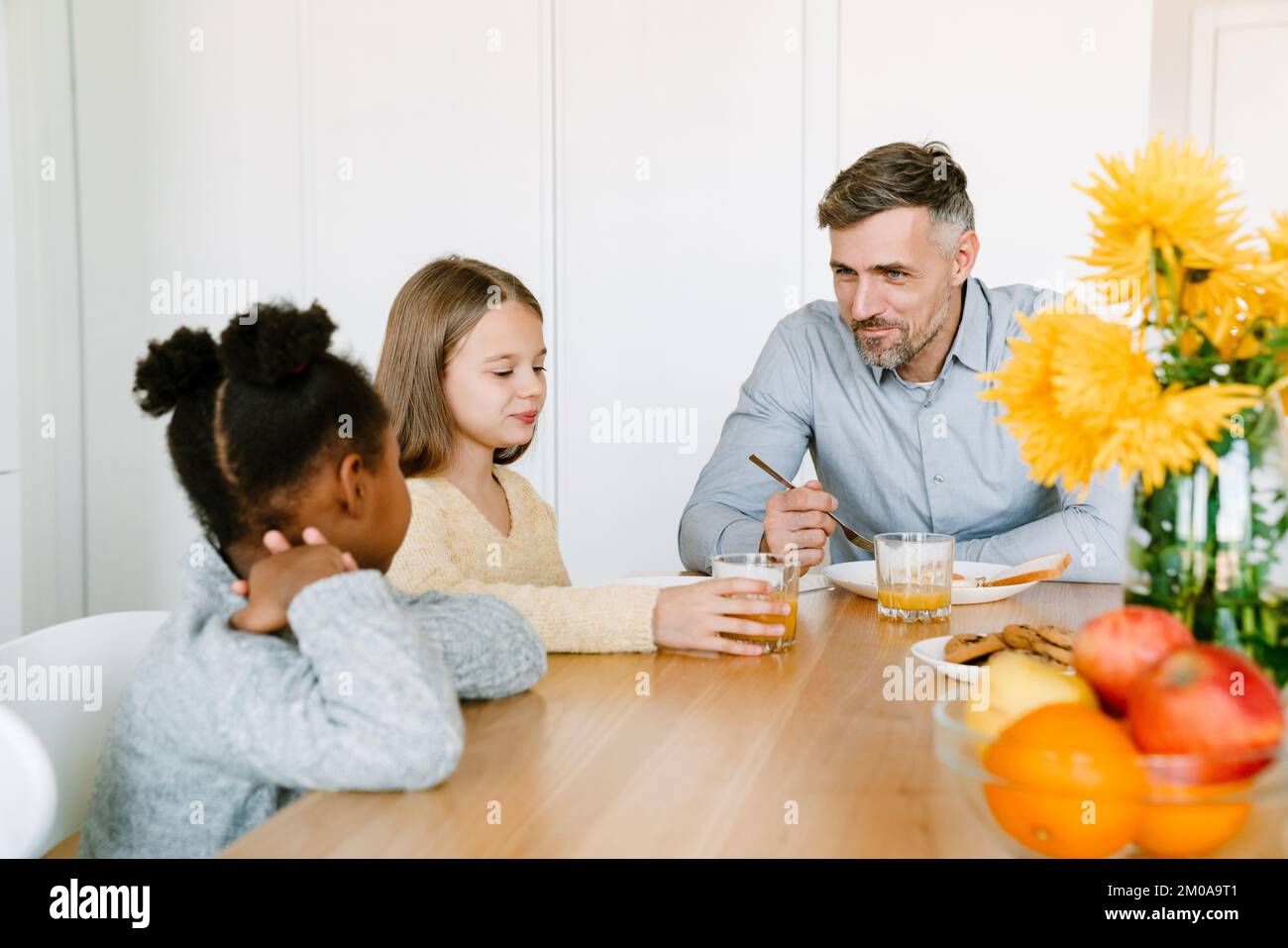 Smiling father having breakfast with interracial daughters. Adoption concept. Stock Photo