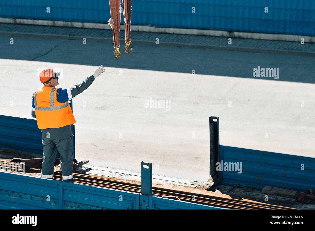 Slinger in helmet and vest unloads metal pipes and fittings from truck