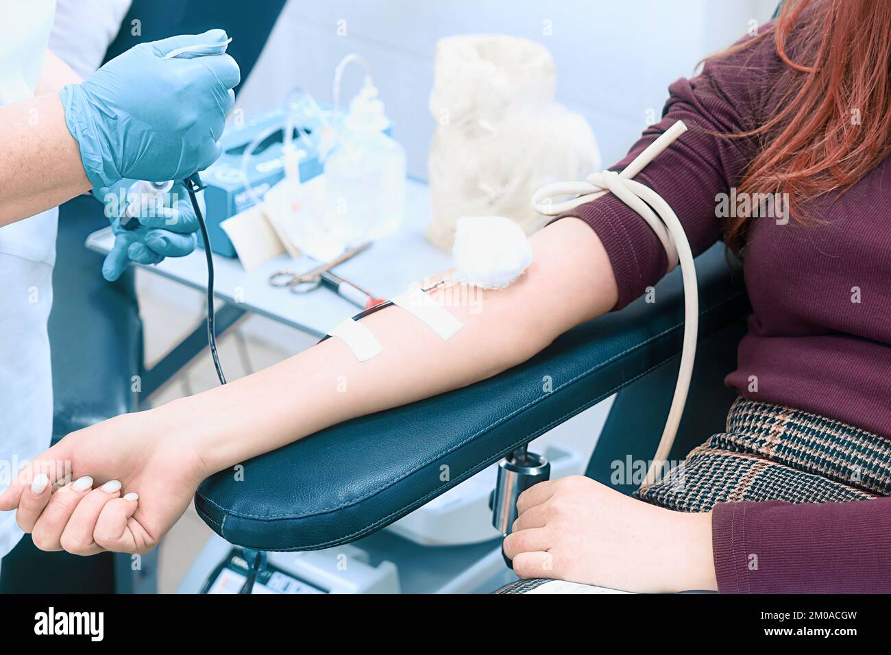 Health worker takes blood from woman's vein. Topic of donation. Female donor sitting in medical chair. Female hand with close-up dropper.. Stock Photo