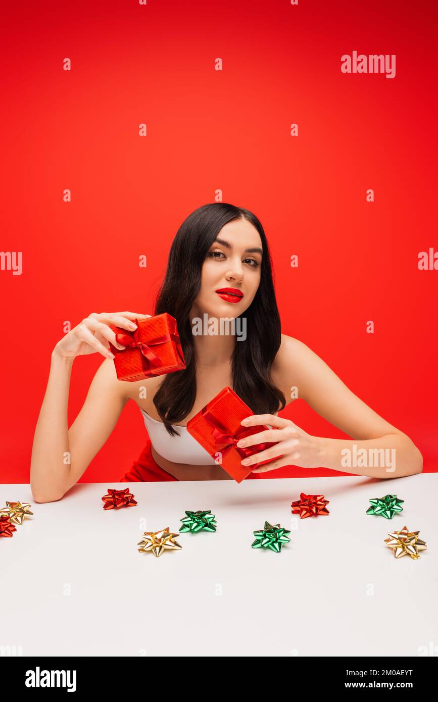 Pretty model with visage holding presents near gift bows isolated on red Stock Photo