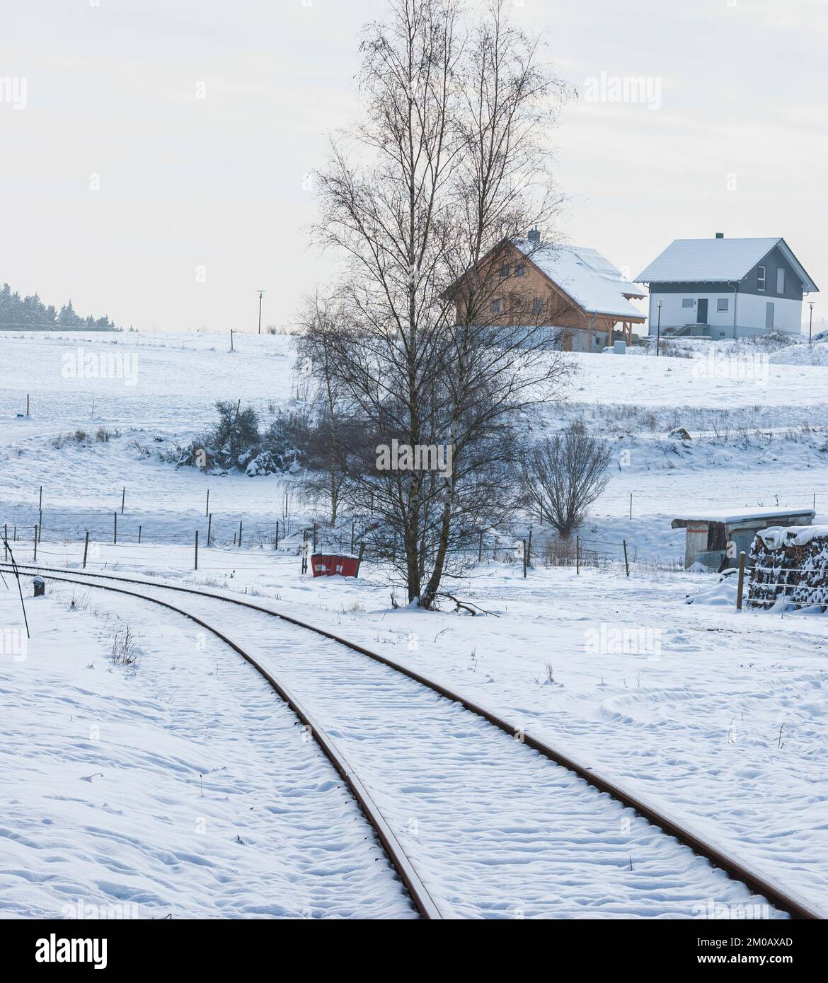 Railway tracks run through the snowy and wintry rural village landscape ...