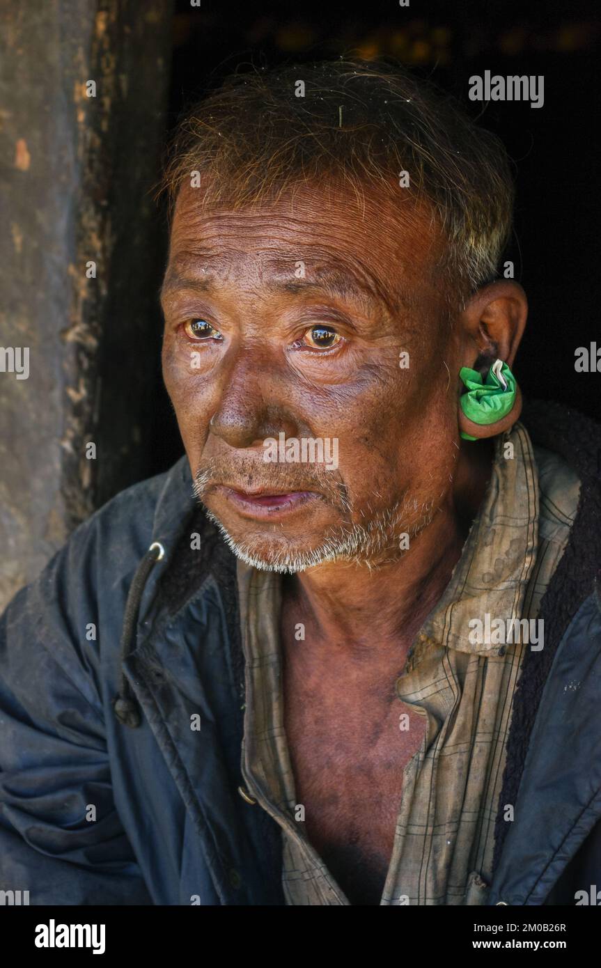 Mon district, Nagaland, India - 11 19 2010 : Closeup three quarter portrait of old Naga Konyak tribe man with big ear piercing holding tobacco bag Stock Photo