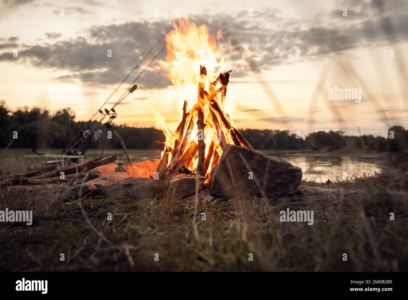 Campfire at a lake with fishing gear in the background Stock Photo