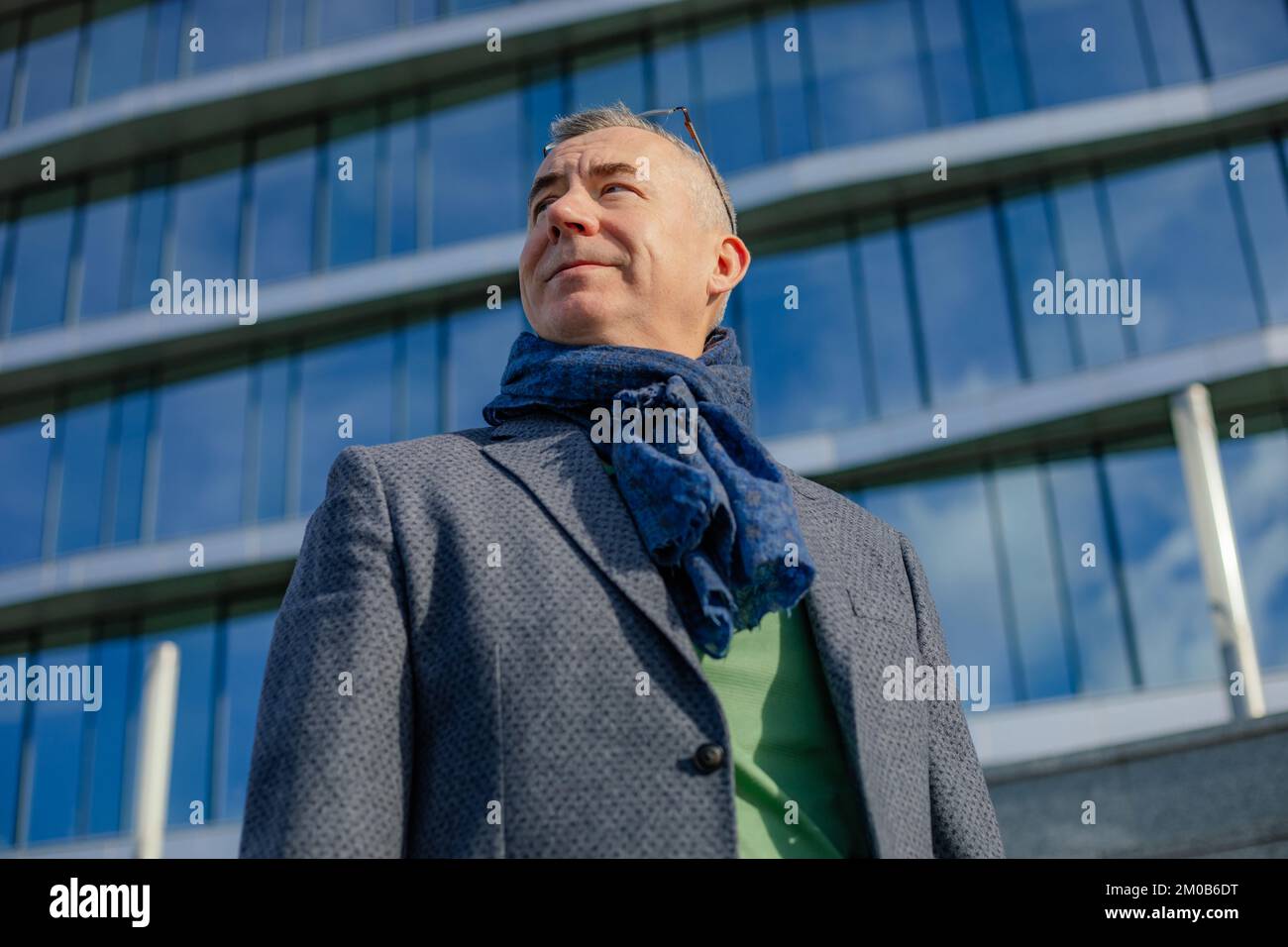 Portrait of smiling middle-aged man standing near modern building, walking outside in city on sunny day in autumn. Stock Photo