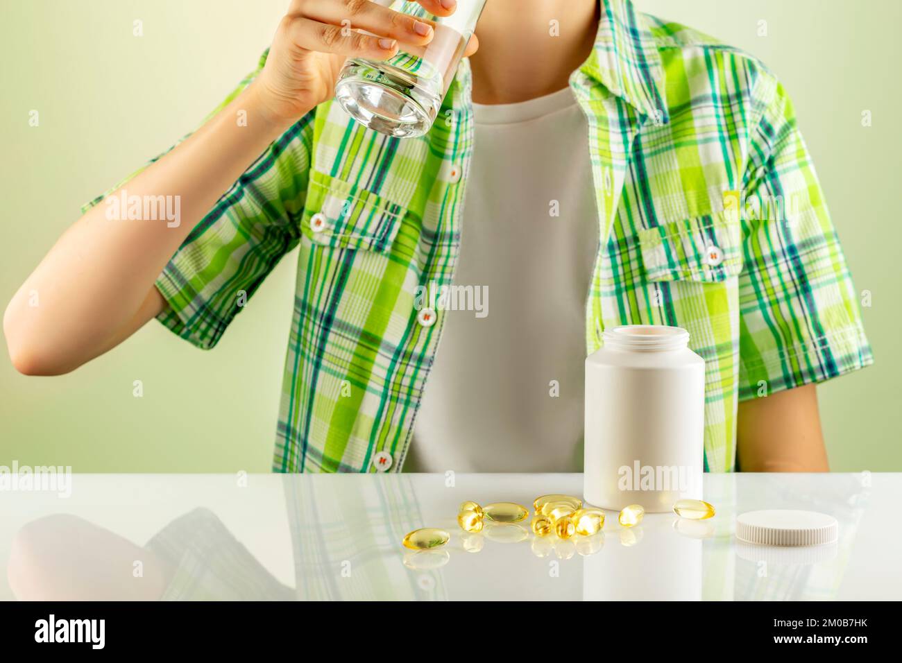 Organic kids vitamins and nutrients. Mockup of natural bio pills, vitamins or supplements. The boy washes down vitamins in gel capsules with water. Su Stock Photo