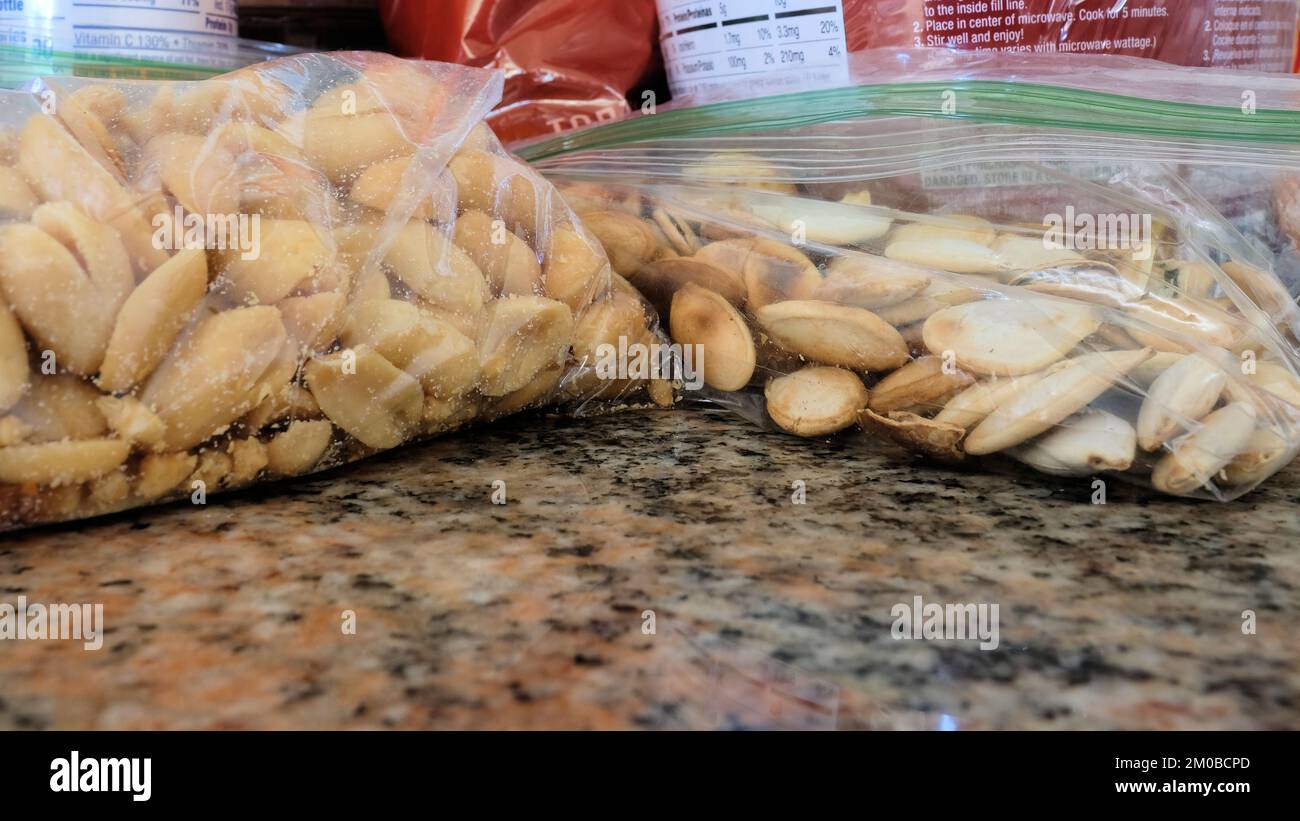 Close-up of two plastic zip bags with roasted salted peanuts and roasted salted pumpkin seeds on kitchen counter packed for snacking, hiking, camping. Stock Photo