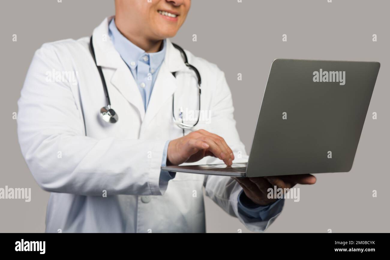 Happy mature chinese male therapist in white coat with stethoscope typing on computer, cropped, close up Stock Photo