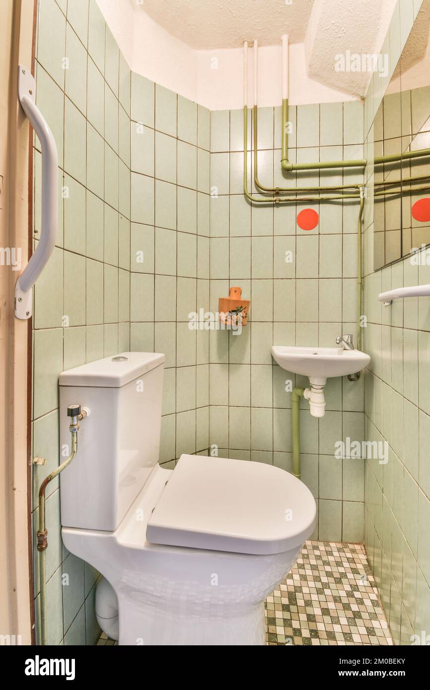 Flush toilet and ceramic sink installed on walls in narrow restroom at