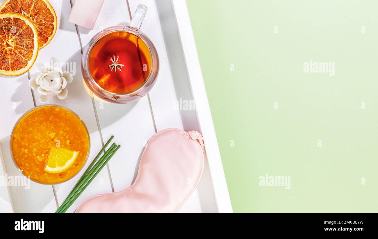 Sleep care banner with mask for sleep, cup of tea, orange jam, aroma sticks on wooden tray with copy space. Concept of relax, self care and me time. I Stock Photo