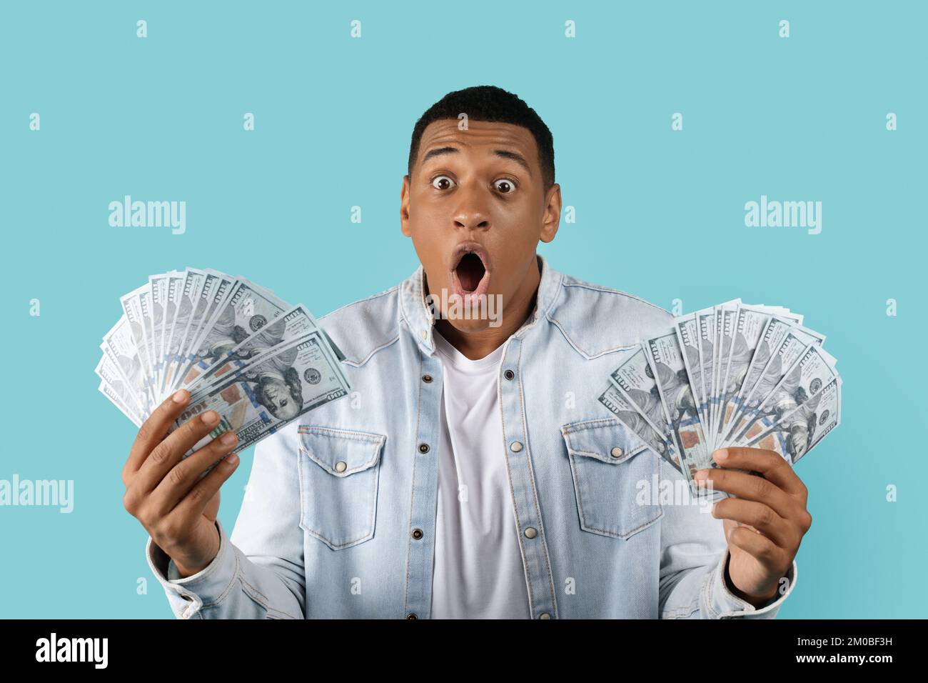 Shocked glad excited funny young african american man with open mouth look at many dollars in hands Stock Photo