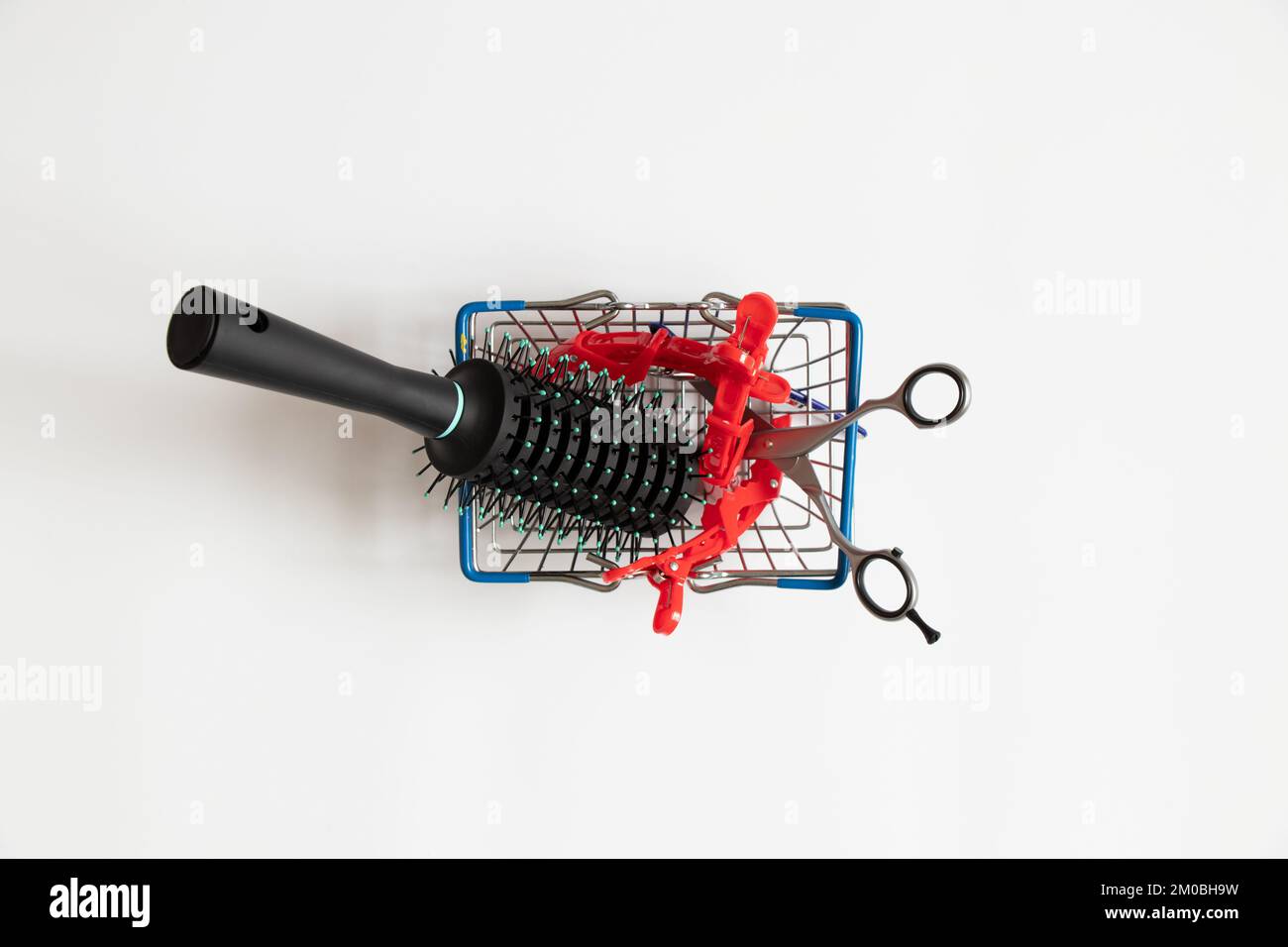 Scissors and a hair clip and a comb lie in a supermarket basket on a white background, a hairdresser's set, business and services Stock Photo