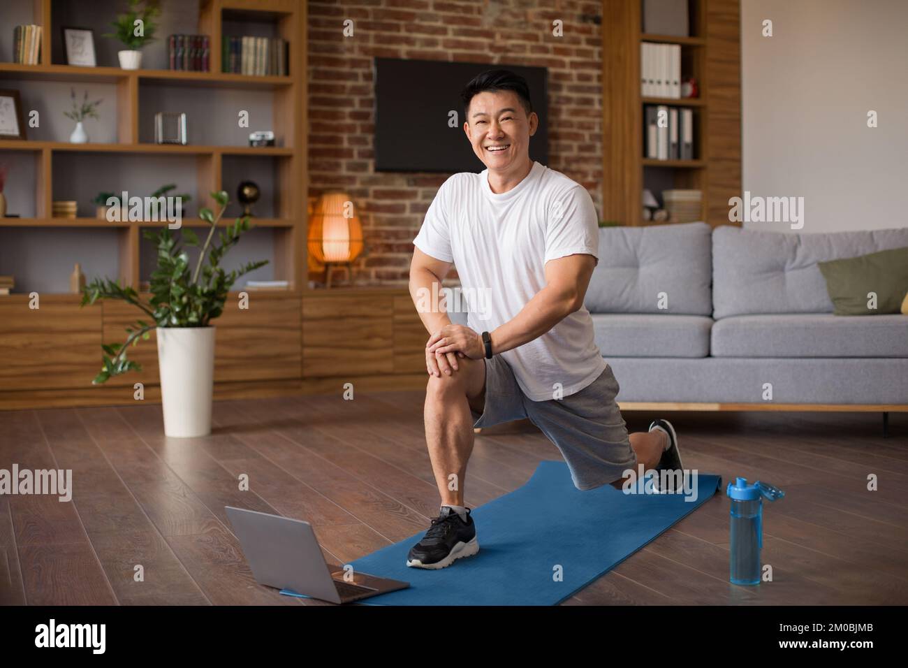 Excited mature korean man doing lunges, exercising for legs in living