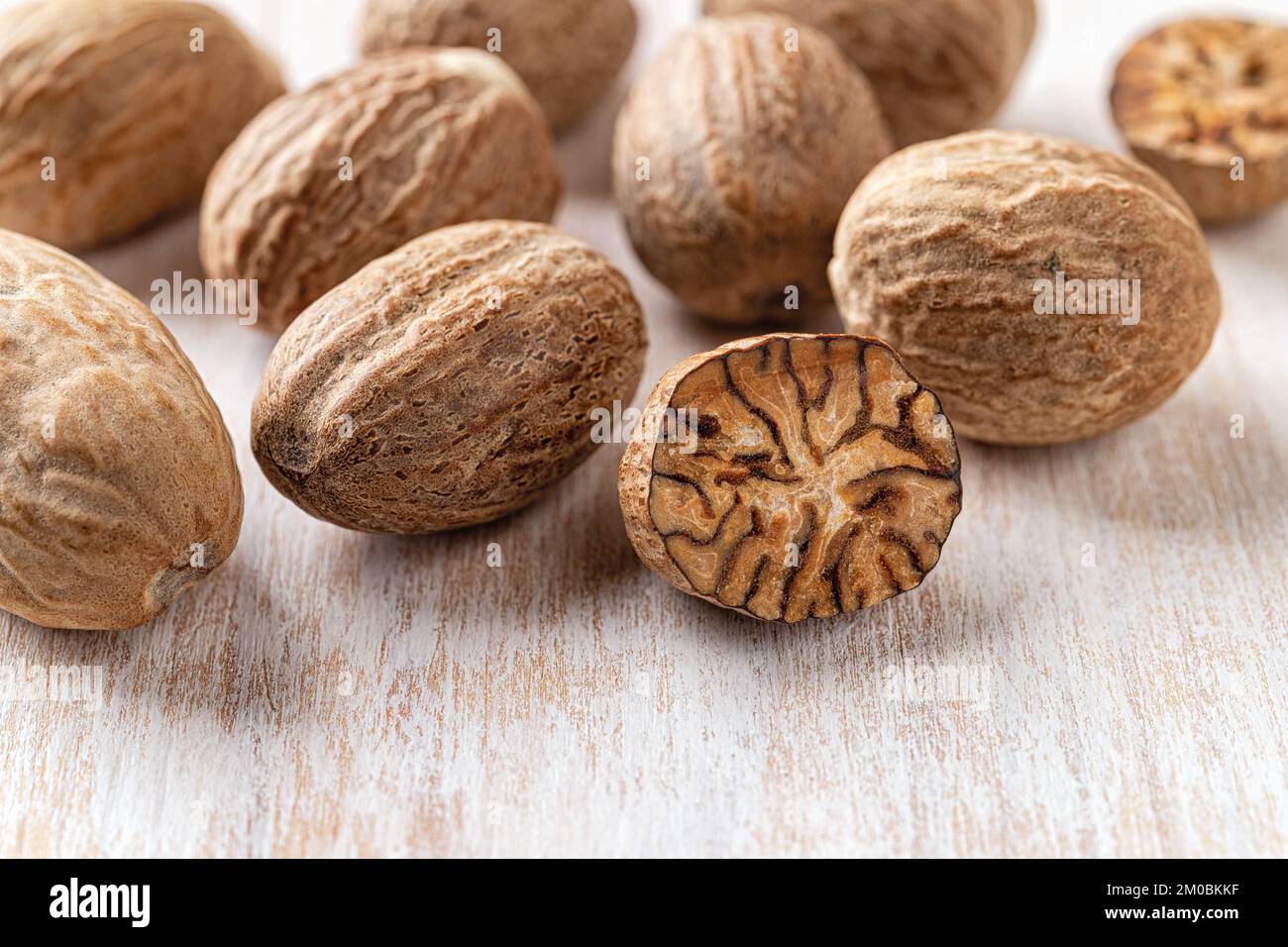 Whole and halved nutmeg seeds over white wooden background macro