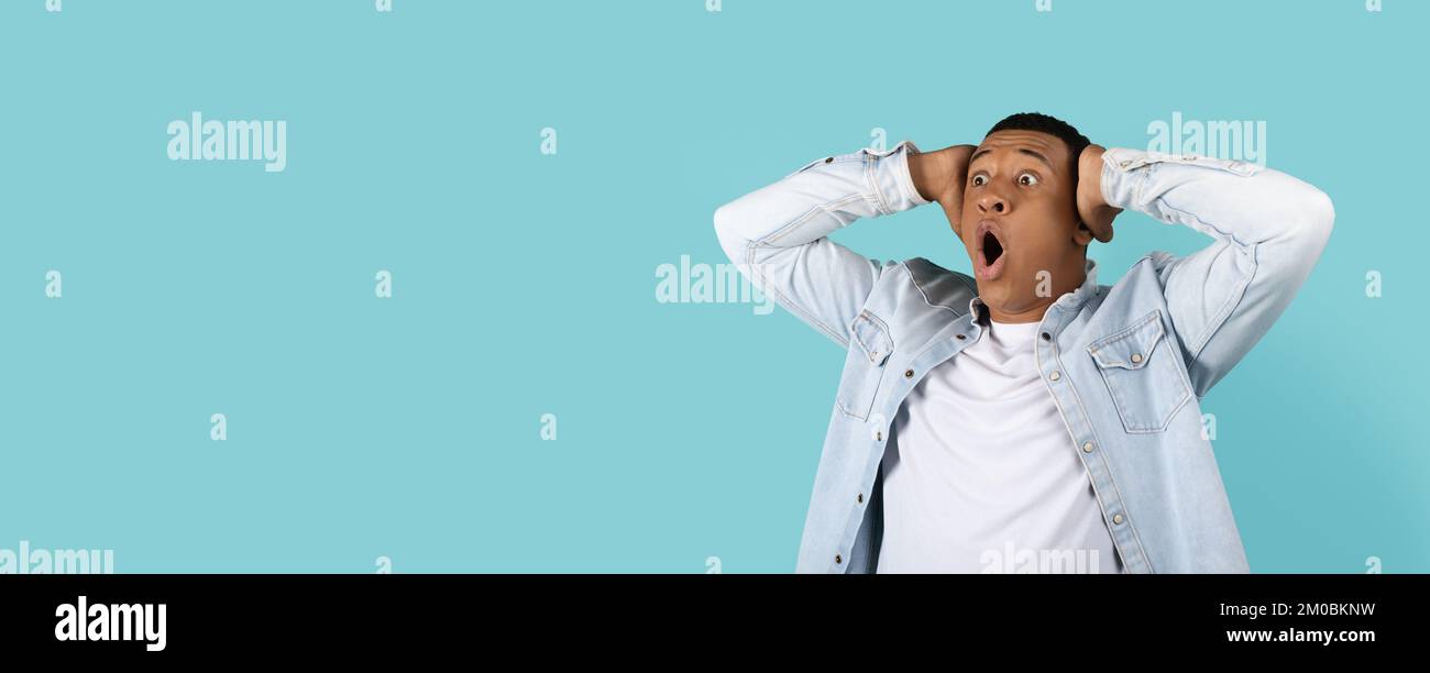 Shocked funny young african american man with open mouth hold his head and screaming Stock Photo