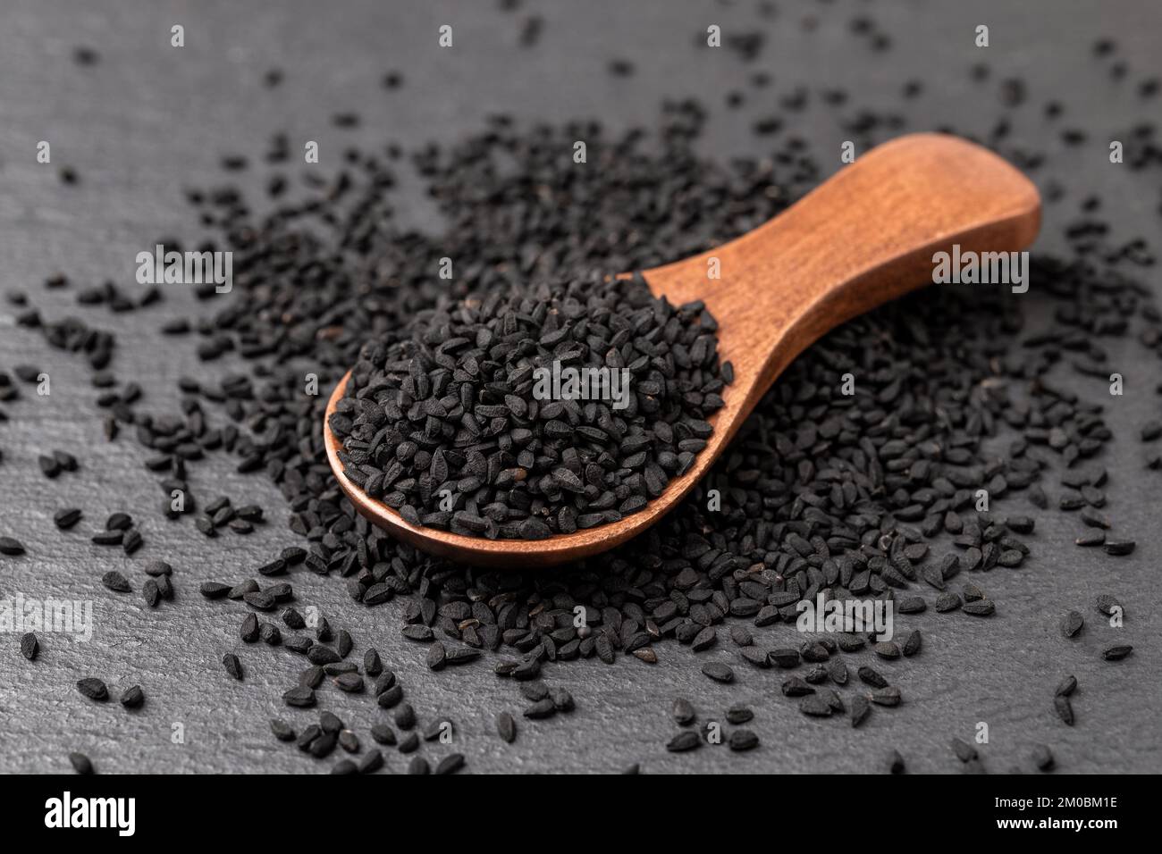 Black cumin seeds in a wooden spoon over black background. Nigella sativa for Ayurveda and herbal medicine and. Kalonji seeds for cooking. Macro. Stock Photo