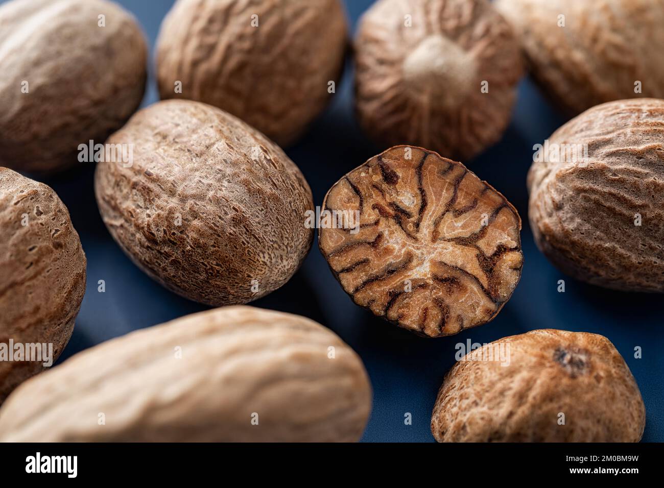 Whole and halved nutmeg seeds over blue background. Macro. Muscat nuts