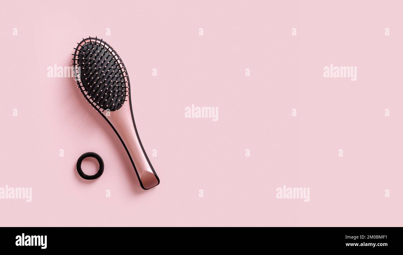 Black pink paddle hair brush against pastel pink background. Stylish wet detangler brush for combing, detangling and hair care concept. Hairdressing. Stock Photo
