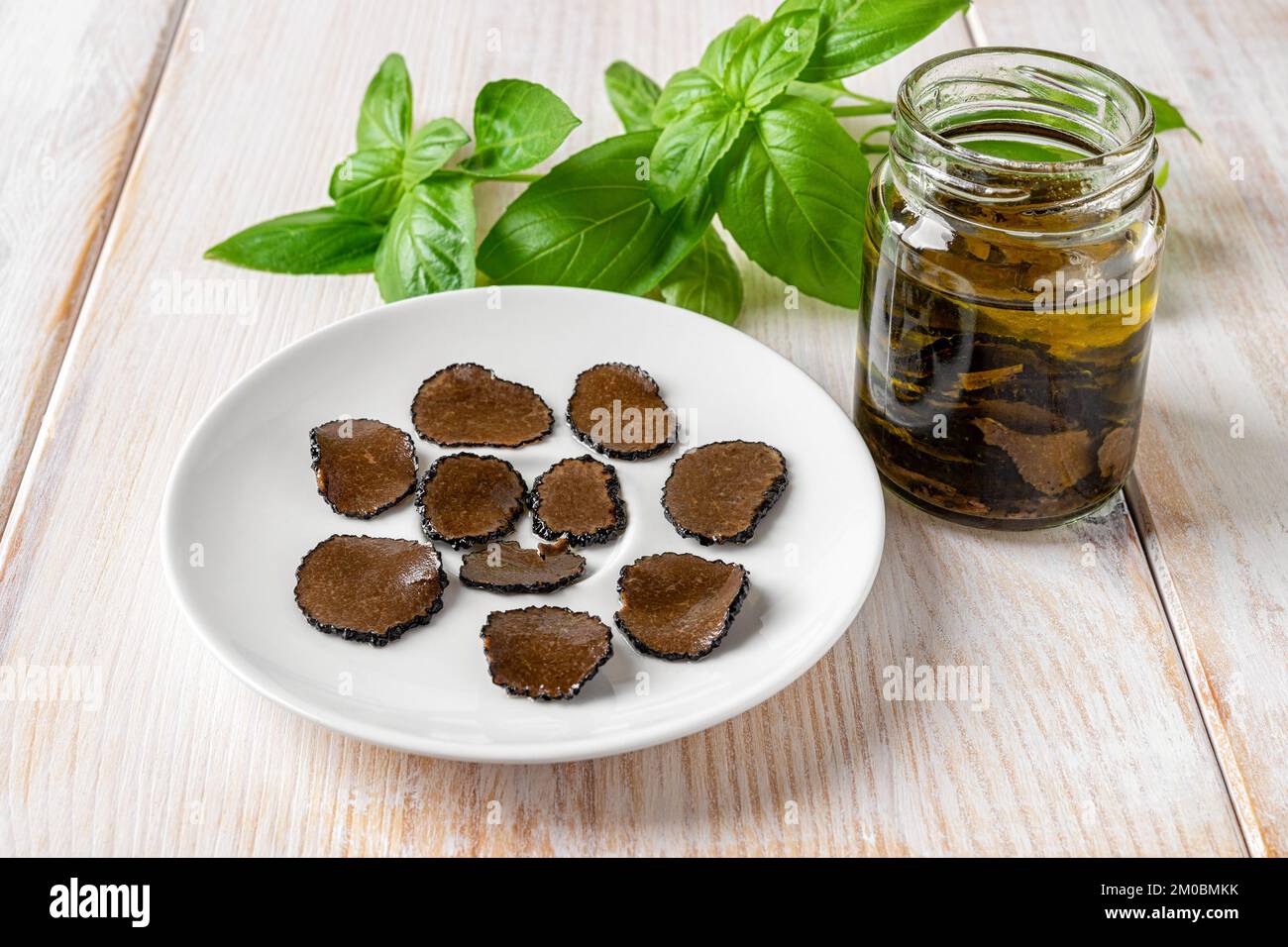 Truffle carpaccio slices on a plate and jar of sliced black truffle in oil over white wooden