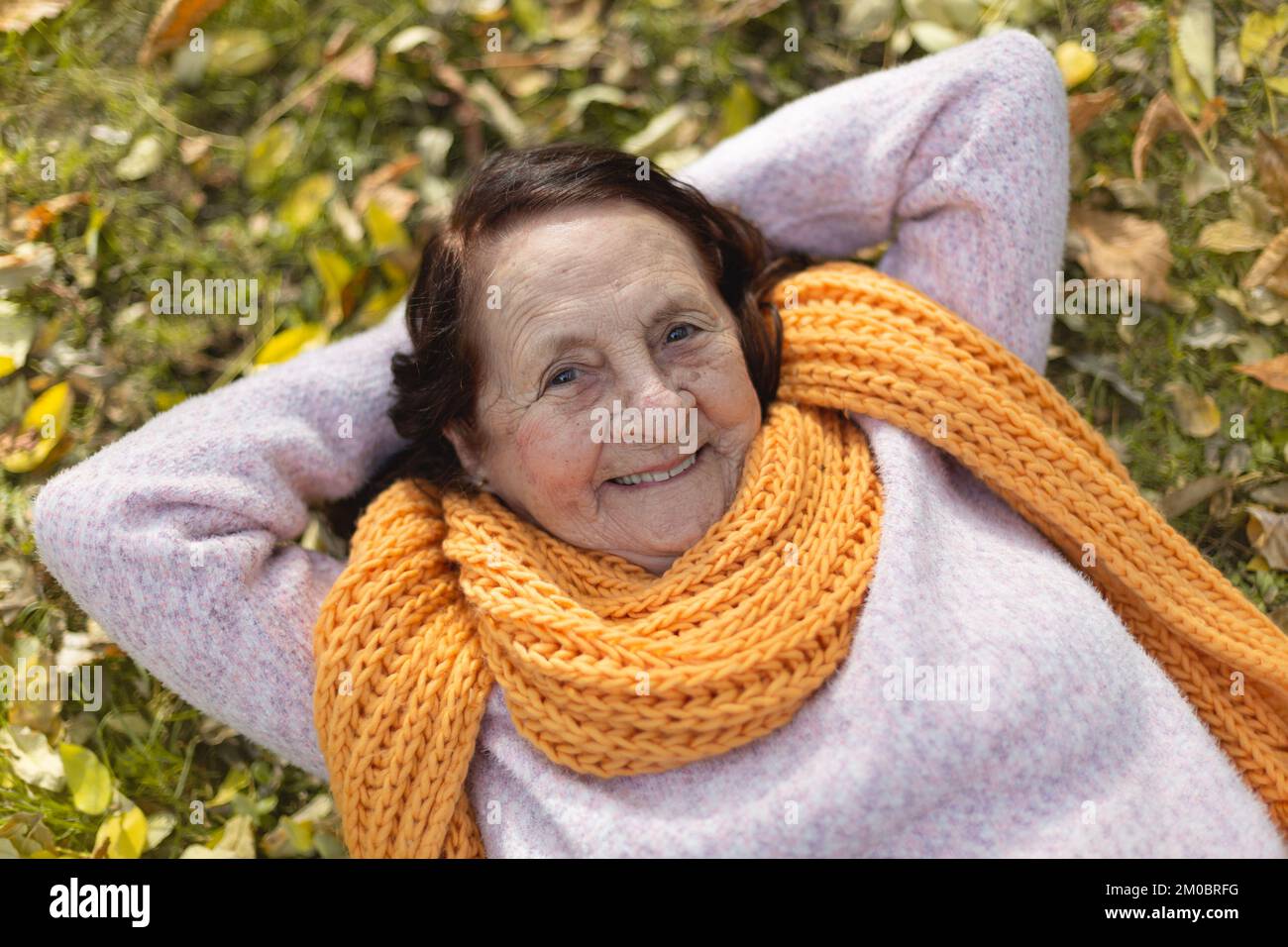 Portrait of happy old Caucasian lady outdoors. She is lying on the grass. Stock Photo