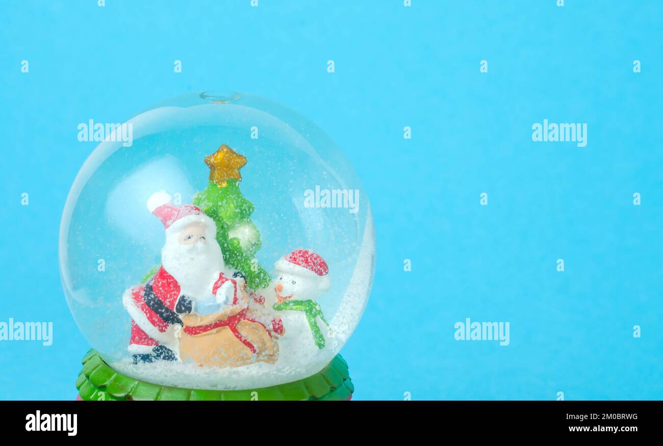 Blue Christmas background with snow globe with Santa, snowman and Christmas tree with copy space. Stock Photo