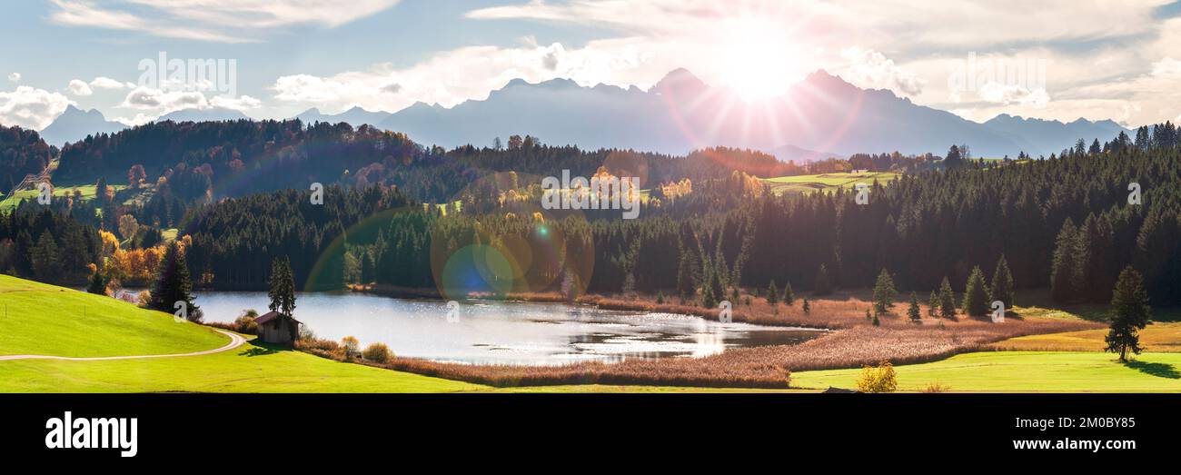 panoramic landscape with lake aund mountainrange against sky with sun Stock Photo