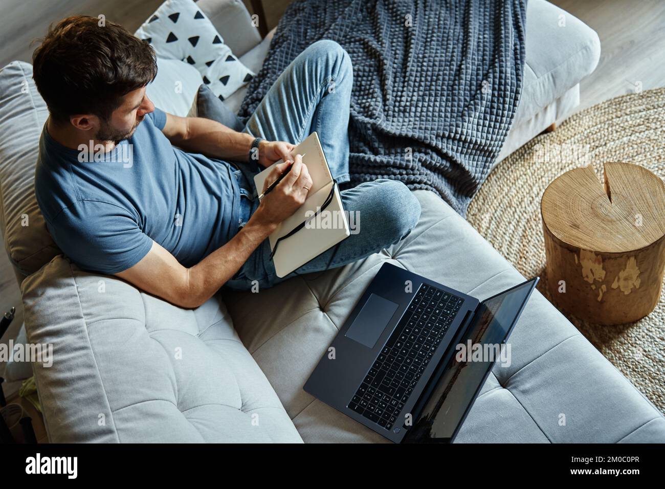 Above view of man sitting on sofa and using laptop. Freelancer working at home workplace. Remote work and work from home concept Stock Photo