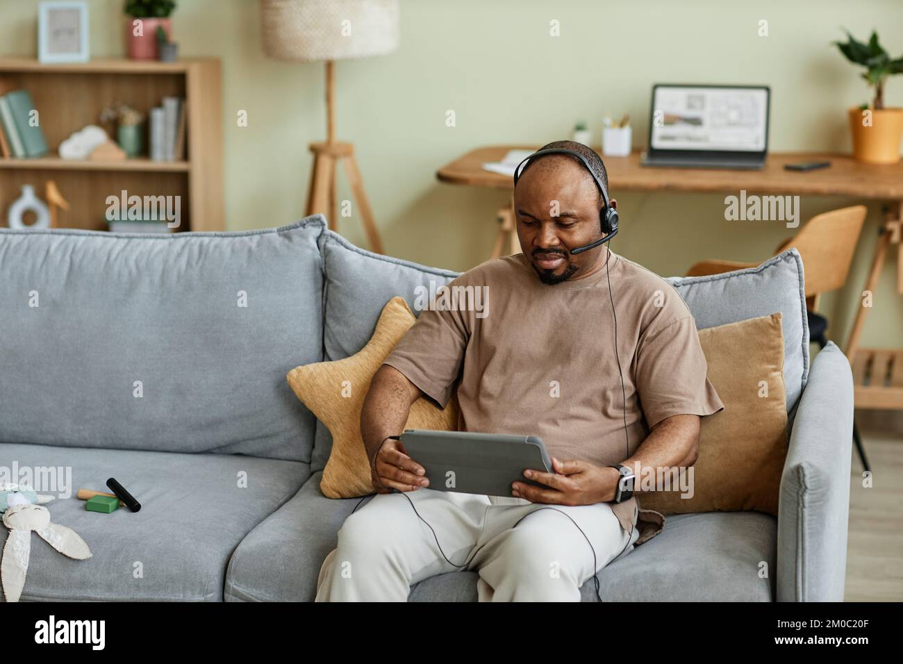 Portrait of adult black man wearing headset using video chat via tablet in cozy home interior, copy space Stock Photo