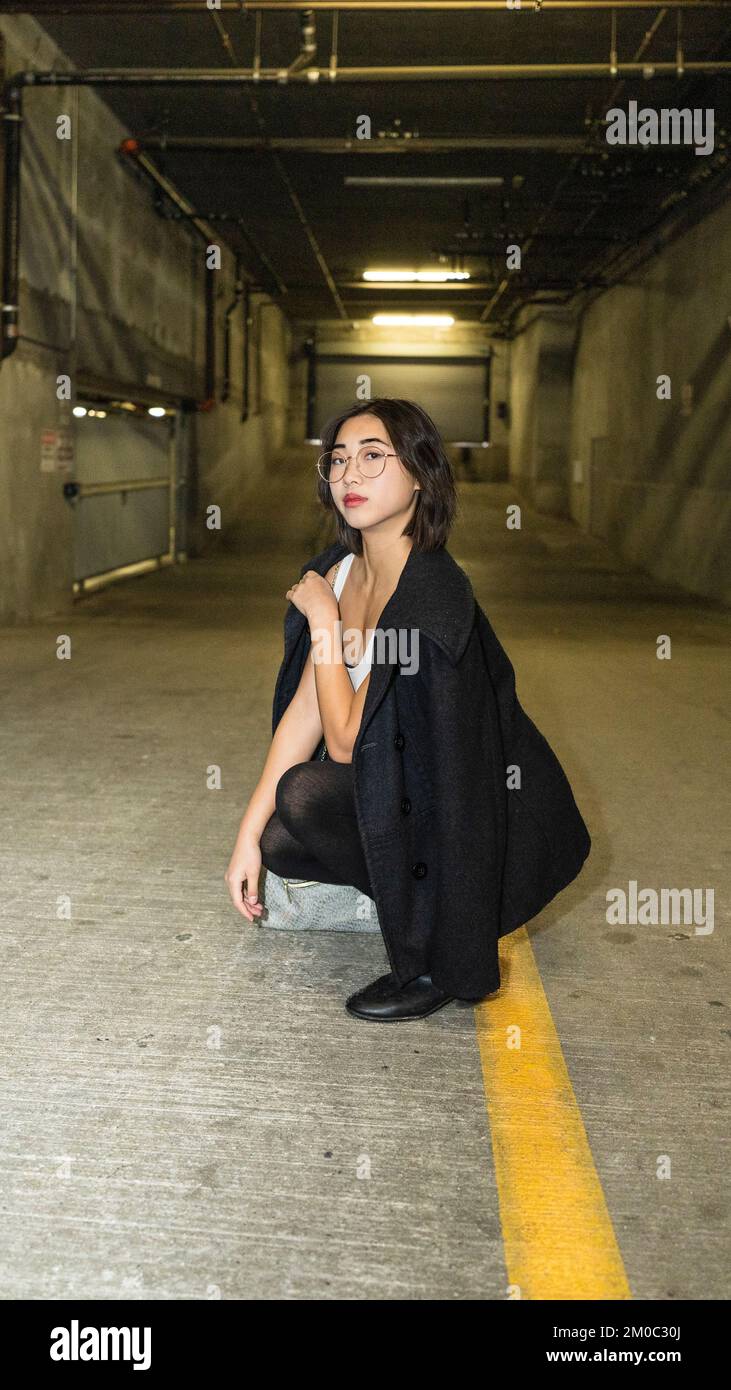 Young Woman Wearing Business Casual Attire Squatting on a Parking Garage Ramp Stock Photo