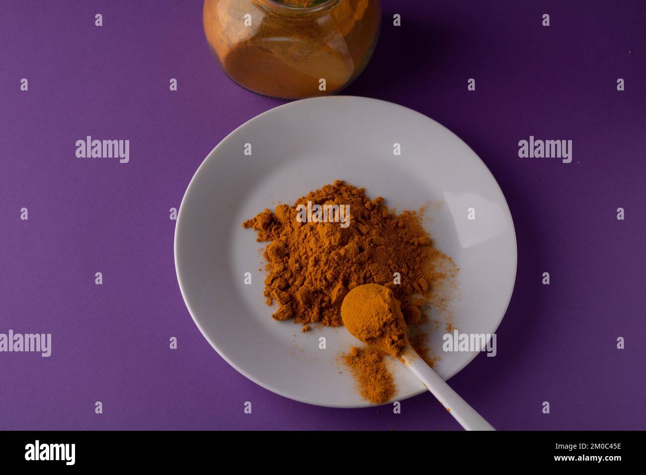 photo turmeric spice piled on a round white plate on a purple background Stock Photo