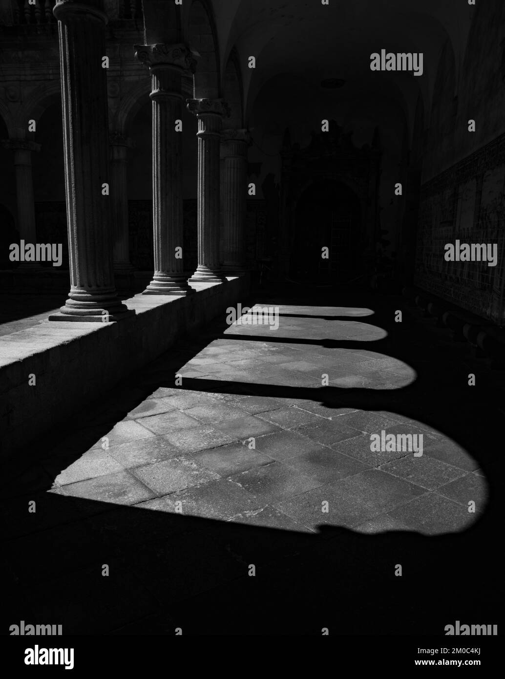 Ornate medieval arches that generate their own shadow and silhouette. Behind the cloister and the blue tile panels that cover the walls of the cloiste Stock Photo